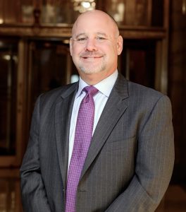 Man wearing gray suit and purple tie while smiling