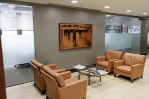 Office waiting room with four brown leather chairs and a glass coffee table