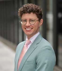 Person standing outside and smiling while wearing gray suit and pink tie