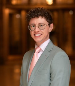 Person smiling and wearing gray suit and pink tie