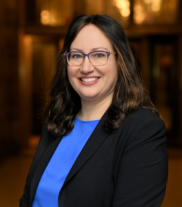 Woman in dark blue suit jacket and light blue shirt.