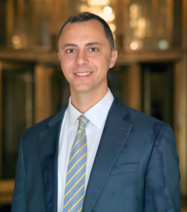 Man in blue suit jacket and shirt and tie standing in front of library books