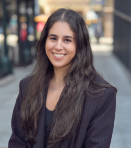 Person wearing black business suit standing on a street with blurred background